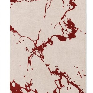 Puede incluir: Una alfombra rectangular con una base de color crema y un patr&oacute;n abstracto audaz en rojo oscuro que se asemeja a vetas de m&aacute;rmol o salpicaduras org&aacute;nicas. La superficie tiene una textura de pelo denso y uniforme en todo el dise&ntilde;o.