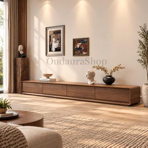 May include: A long, low-profile wooden media console featuring four rectangular drawers with a smooth, dark brown wood grain finish and rounded edges, positioned against a light-colored wall with the text OudauraShop visible in the center.