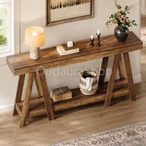May include: A long, rectangular wooden console table with a dark brown finish and an A-frame leg design. The table features a lower shelf, a flat top surface, and a sturdy construction. The wood grain is visible throughout the entire furniture piece.