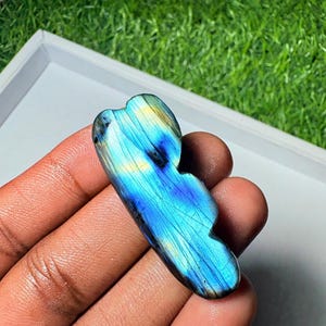 May include: A polished labradorite stone featuring a vibrant iridescent blue and yellow flash across its surface. The stone has an irregular, organic shape with smooth, rounded edges and visible internal fractures that catch the light.