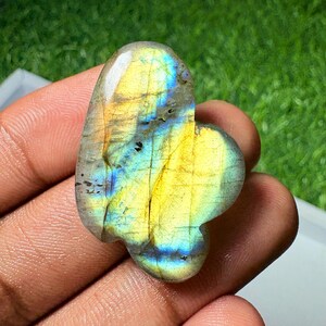 Peut inclure: Une pierre précieuse de labradorite polie avec une forme arrondie irrégulière. La pierre présente un effet de labradorescence vibrant, avec des éclats iridescents de jaune vif et de bleu électrique sur sa surface grise lisse et semi-translucide.