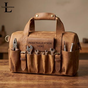May include: A brown leather tool bag featuring a top handle, two side buckles, and multiple exterior pockets. The front flap is embossed with the text PERSONALIZATION HERE and contains various metal tools including pliers and wrenches.