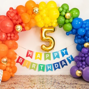 May include: A rainbow-colored balloon arch featuring red, orange, yellow, green, blue, and purple balloons with gold accents. A large gold foil balloon in the shape of the number 5 is centered. A banner with the text HAPPY BIRTHDAY is displayed.