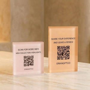 Könnte beinhalten: Zwei rechteckige Acrylschilder mit matter Oberfläche. Das kleinere quadratische Schild ist hellrosa mit dem Text SCAN FOR MORE INFO NEW COLLECTION HIGHLIGHTS und einem QR-Code. Das größere Schild ist pfirsichfarben mit SHARE YOUR EXPERIENCE AND LEAVE A REVIEW und einem QR-Code. Beide tragen den Text ERIKAGIFTCO.