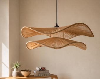 May include: A double-tiered pendant light fixture featuring two wide, wavy, tan-colored shades constructed from tightly wound cord. The fixture is suspended by a thin black cord and features a central black mounting piece connecting the two tiers.