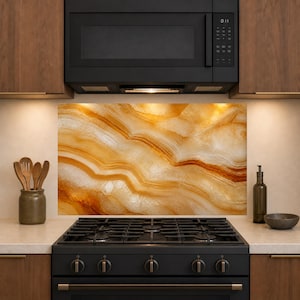 May include: A rectangular kitchen backsplash panel featuring a high-resolution print of golden-brown onyx stone with swirling, layered patterns. The panel is installed behind a black gas stove and below a black microwave, set between wooden cabinets.
