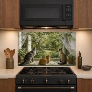 May include: A kitchen backsplash panel featuring a printed scene of three cats sitting on a windowsill looking out at a garden with a small deer. The cats are a grey tabby, an orange tabby, and a Siamese. White curtains frame the garden view.
