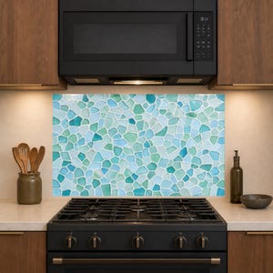 May include: A kitchen splashback featuring a mosaic of irregular, smooth-edged glass tiles in various shades of seafoam green, turquoise, and white, arranged in a random pattern behind a black gas stove and a black microwave oven.