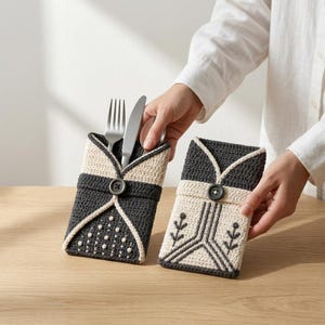 May include: Two rectangular crochet cutlery holders featuring a fold-over design secured with a single button. One holder is dark gray with cream accents and dotted patterns, while the other is cream with dark gray geometric and floral embroidery.