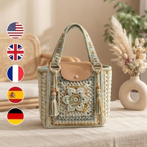 May include: A crochet handbag featuring a square floral motif in shades of sage green, cream, and mustard yellow. The bag includes a tan leather flap closure with a snap button, two sturdy crochet handles, and two hanging tassels with wooden beads.