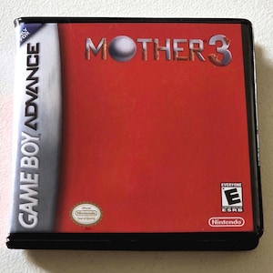 May include: A rectangular video game case for the Game Boy Advance featuring a bright red cover with the title MOTHER 3 in metallic lettering. The case includes the Nintendo logo, an ESRB E rating for everyone, and an official Nintendo seal.