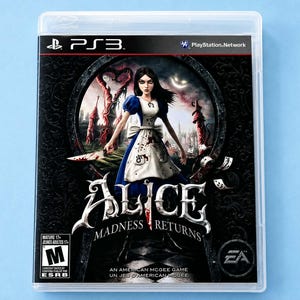May include: A PlayStation 3 video game case for Alice: Madness Returns. The cover art features a dark-haired character in a blue and white dress holding a blood-stained knife, standing before a keyhole-shaped portal with surreal, twisted structures.