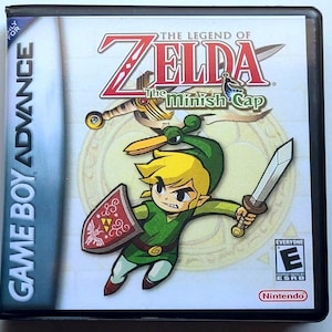 May include: A Game Boy Advance video game case for The Legend of Zelda: The Minish Cap. The cover features a cartoon character with blonde hair wearing a green tunic and hat, holding a sword and a red shield with a gold emblem, with the game title.