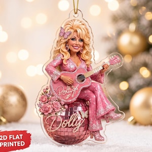 May include: A flat acrylic ornament featuring a blonde figure in a pink rhinestone-embellished suit, playing a pink acoustic guitar with the name Dolly printed on it. The figure sits on a pink disco ball with the name Dolly and pink roses.