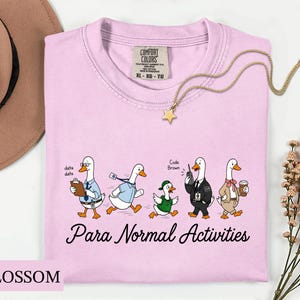 Puede incluir: Una camiseta rosa claro con un gráfico de cinco patos de dibujos animados vestidos con varios atuendos profesionales. El texto "Para Normal Activities" está impreso debajo de los patos. La camiseta tiene una etiqueta Comfort Colors en el cuello y es talla XL.