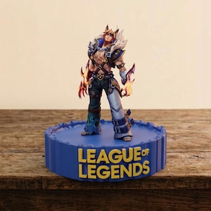May include: A collectible figurine of a character with animal-like ears, wearing a dark blue and white outfit with orange glowing gauntlets, standing on a circular blue base with the yellow text LEAGUE OF LEGENDS printed on the front side.