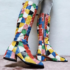 Könnte beinhalten: Kniehohe Stiefel mit einem lebendigen, geometrischen Muster in Rot, Gelb, Blau, Grün und Schwarz. Die Stiefel haben einen Blockabsatz und einen seitlichen Reißverschluss. Die Stiefel sind ca. 35.5 cm hoch.