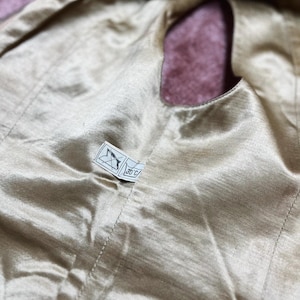 May include: Close-up of a gold satin fabric with a small label attached. The fabric has a smooth, shiny texture and a small opening. The label has a symbol and the text "30 C".