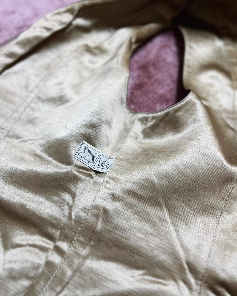May include: Close-up of a gold satin fabric with a small label attached. The fabric has a smooth, shiny texture and a small opening. The label has a symbol and the text "30 C".