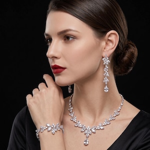 May include: A jewelry set consisting of a silver-toned necklace, a matching bracelet, and long drop earrings. Each piece features clear, marquise-cut and pear-shaped crystals arranged in a floral-inspired pattern with a central teardrop pendant.