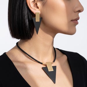 May include: A jewelry set consisting of a necklace and earrings. The necklace features a black cord with a gold-toned rectangular connector attached to a black triangular pendant. The earrings match, with a gold-toned rectangle and black triangle.