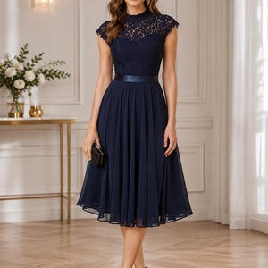 May include: A navy blue midi dress featuring a high-neck lace bodice with cap sleeves and a solid satin waistband. The skirt is made of a flowing, pleated chiffon fabric that falls below the knees, creating a structured yet elegant silhouette.