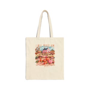 Peut inclure: Un sac fourre-tout en toile beige avec une illustration colorée d'une maison rose entourée de citrouilles orange et roses dans un champ. Le texte "I WILL PRAISE HIM IN EVERY SEASON" est imprimé au-dessus et en dessous en police brune.