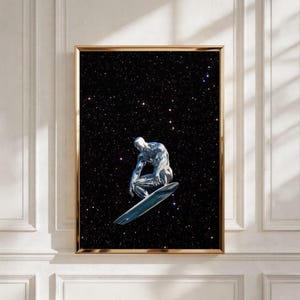 Op de afbeelding: Een ingelijste wandkunstprint met een metallic zilveren mensachtige figuur in een gehurkte houding, balancerend op een slanke surfplank. De figuur staat tegen een diepzwarte achtergrond vol met talloze kleine, helderwitte sterren in de ruimte.