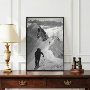 Puede incluir: Una impresión de arte mural enmarcada en blanco y negro que representa una cresta de montaña nevada con dos figuras caminando. En primer plano se ve a un escalador con equipo, mientras que una segunda figura más pequeña se ve más arriba.