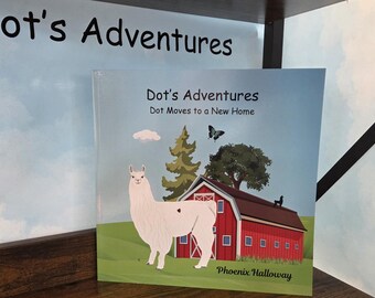 Op de afbeelding: Een vierkant kinderboek getiteld Dot's Adventures: Dot Moves to a New Home door Phoenix Halloway. De kaft toont een witte lama met een donkere vlek, een rode schuur, een groene boom, een vlinder en een klein wolkje tegen een lichtblauwe lucht.