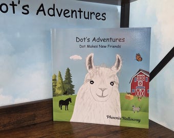 Op de afbeelding: Een vierkant kinderboek getiteld Dot's Adventures: Dot Makes New Friends door Phoenix Halloway. De kaft toont een illustratie van een witte lama tegen een boerderijlandschap met een rode schuur, groen gras, bomen en een vlinder in een blauwe lucht.
