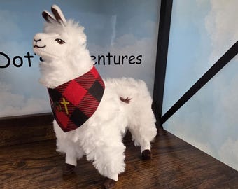 Op de afbeelding: Een witte pluche lama met een rood en zwart geruite bandana om de nek. De bandana is voorzien van een klein geel kruis-embleem. De tekst Dot's Adventures is zichtbaar op de achtergrond achter de lama-figuur.