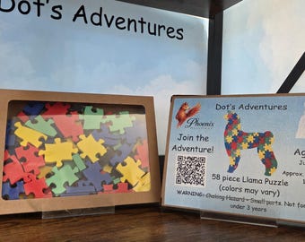 Op de afbeelding: Een 58-delige lamapuzzel in een bruine doos met een doorzichtig venster met kleurrijke puzzelstukjes. Daarnaast staat een kaart met de tekst Dot's Adventures, een lama-afbeelding, een QR-code en de afmeting van circa 33 cm bij 23 cm.