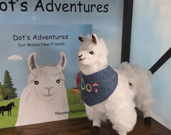 Op de afbeelding: Een wit pluche lama-speeltje met een blauwe bandana waarop het woord Dot is geborduurd in meerkleurig garen, naast een kinderboek getiteld Dot's Adventures: Dot Makes New Friends, met een illustratie van een lama.