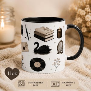 Può includere: Una tazza in ceramica bianca con interno e manico neri, con una capacità di 325 ml. L'esterno presenta illustrazioni di un cigno nero, una pila di tre libri, un disco in vinile, una candela, uno specchio, un calamaio, una penna e dei fiori.