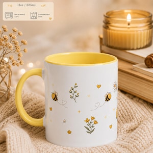 Op de afbeelding: Een witte keramische mok met een gele binnenkant en handvat, voorzien van een patroon van kleine bijtjes, gele bloemen en hartjes. De mok heeft een inhoud van 325ml en is geschikt voor de magnetron en vaatwasser.