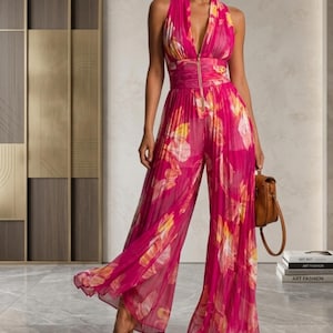 Könnte beinhalten: Ein ärmelloser, plissierter Jumpsuit in leuchtendem Fuchsia-Pink mit tiefem V-Ausschnitt und einem zentralen goldfarbenen Reißverschluss. Das Kleidungsstück zeigt ein abstraktes Blumenmuster in Gelb- und Weißtönen mit weitem Bein.