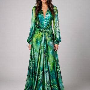 May include: A floor-length long-sleeve dress in shades of emerald, lime, and forest green. The fabric features a botanical leaf print with a deep V-neckline and a central gathered knot detail at the waist, creating a draped, flowing silhouette.