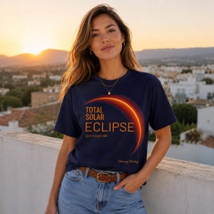 Könnte beinhalten: Ein marineblaues Kurzarm-T-Shirt mit einer Grafik einer leuchtenden Sonnenfinsternis. Der Text lautet Total Solar Eclipse, Spain 12 August 2026 und Chasing Totality. Das Design enthält einen geschwungenen orangefarbenen und gelben Lichtbogen.