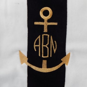 May include: A nautical-themed design featuring a gold embroidered anchor and the initials "ABN" on a black stripe. The background has vertical white stripes. The design is likely for a towel or fabric.