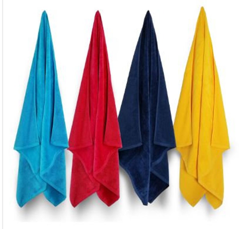 Puede incluir: Cuatro toallas de playa coloridas colgadas sobre un fondo blanco. Las toallas son en tonos azul, rojo, marino y amarillo. Las toallas est&aacute;n dobladas en forma triangular, mostrando su suave textura.