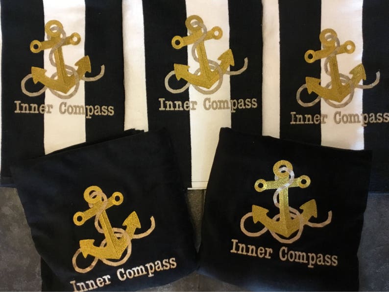Puede incluir: Tela a rayas blancas y negras con dise&ntilde;os de anclas doradas y el texto "Inner Compass". Tambi&eacute;n, tela negra con dise&ntilde;os de anclas doradas y el texto "Inner Compass". Tema n&aacute;utico.