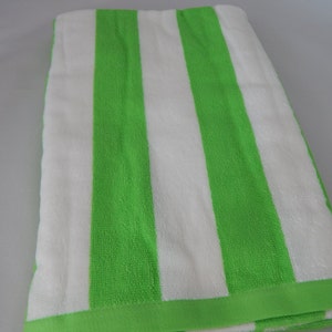 May include: A folded beach towel with wide vertical stripes in bright green and white. The towel has a solid green border along the edges. The fabric appears soft and absorbent, suitable for use at the beach or pool.