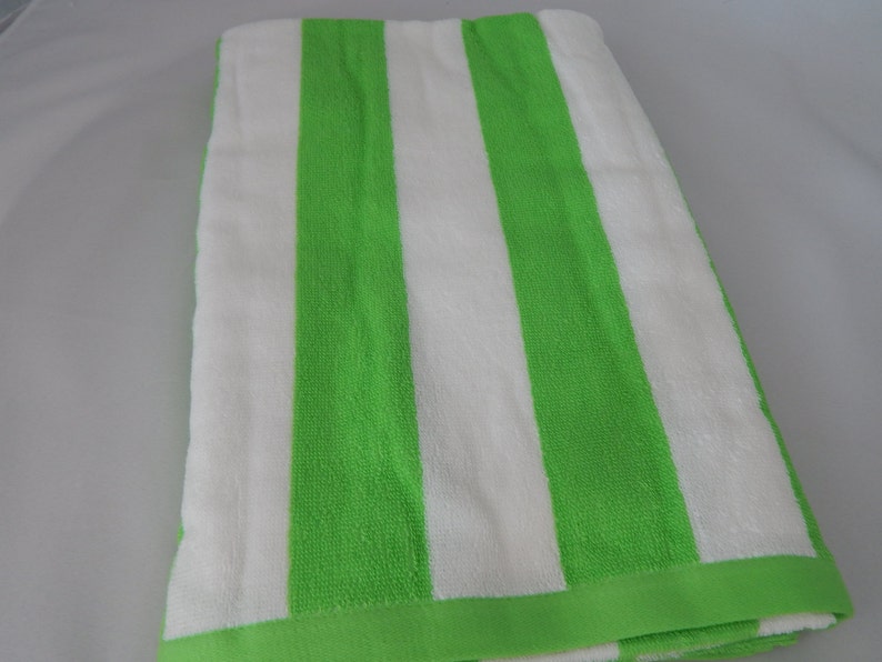 May include: A folded beach towel with wide vertical stripes in bright green and white. The towel has a solid green border along the edges. The fabric appears soft and absorbent, suitable for use at the beach or pool.
