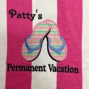 May include: A striped beach towel with alternating pink and white vertical stripes. The towel features an embroidered design of two flip-flops with blue straps and a colorful striped pattern. Text reads "Patty's Permanent Vacation."