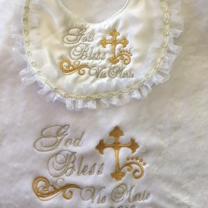 Peut inclure: Ensemble de bavoir et de couverture pour b&eacute;b&eacute; en satin blanc. Le bavoir a un bord &agrave; volants et une broderie dor&eacute;e avec l'inscription "God Bless Via Marie" et une croix. La couverture est brod&eacute;e avec la date "April 8th, 2018".