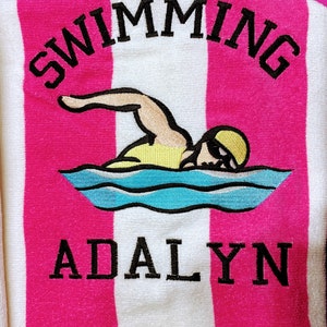 May include: A pink and white striped beach towel with the word "SWIMMING" embroidered in black at the top. Below is an embroidered swimmer graphic and the name "ADALYN" in black. The towel is made of a soft, absorbent material.