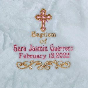 May include: Embroidered baptismal design on a white, textured fabric. The design includes a gold and pink cross, the words "Baptism of Sara Jasmin Guerrero February 12, 2022," and gold floral accents.