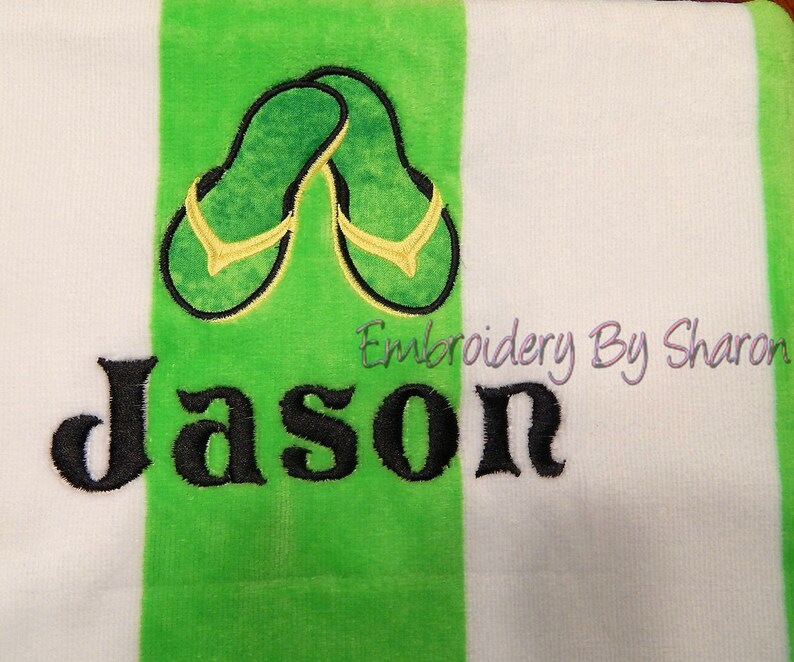 May include: White and green striped beach towel with an embroidered design of green and yellow flip-flops. The name "Jason" is embroidered in large black letters. The text "Embroidery By Sharon" is also visible.