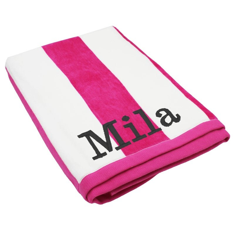 May include: A folded beach towel with a bold pink and white striped pattern. The word "Mila" is embroidered in black block letters on the towel. The towel has a pink border.
